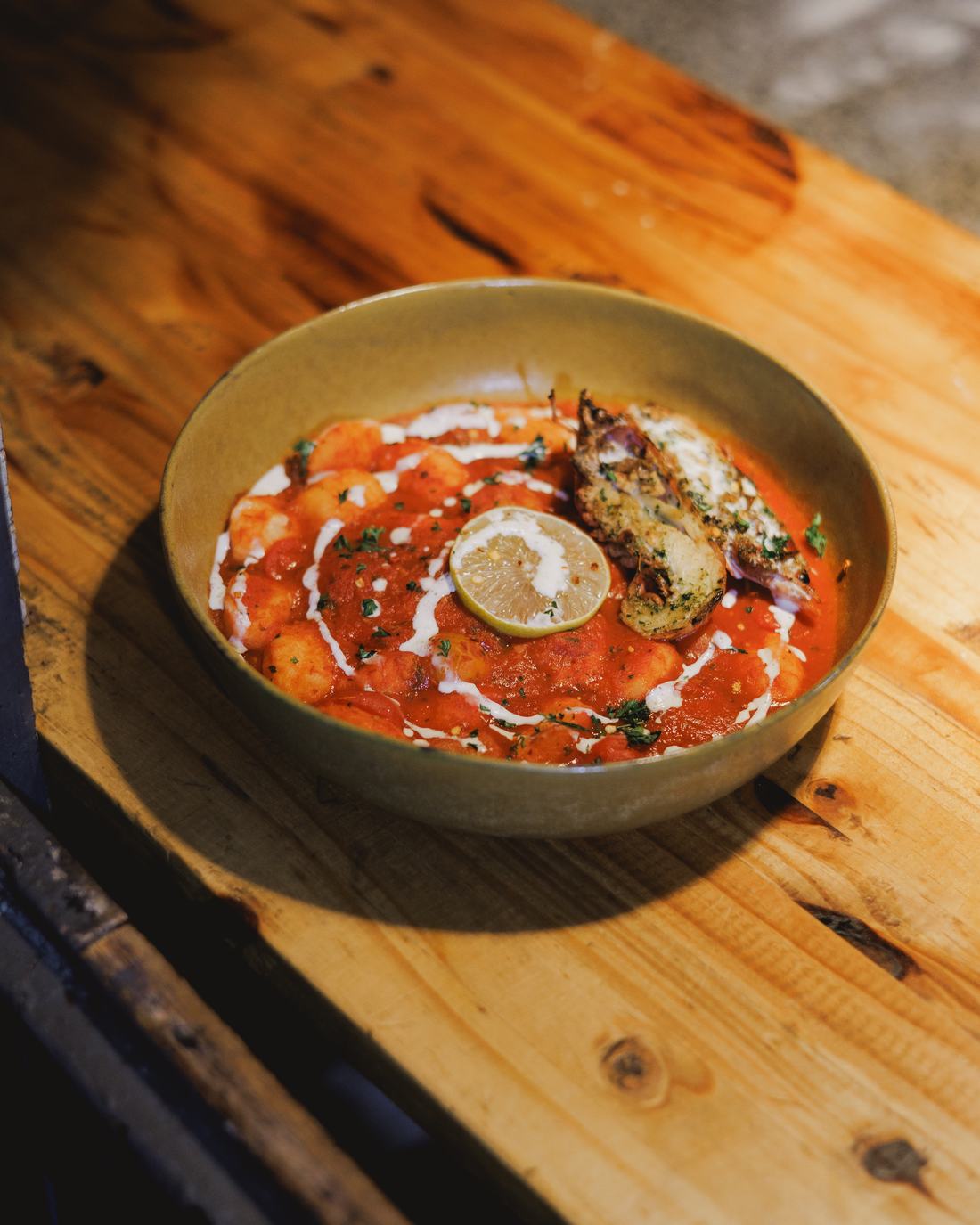 A bowl of pasta in tomato sauce on a wooden board