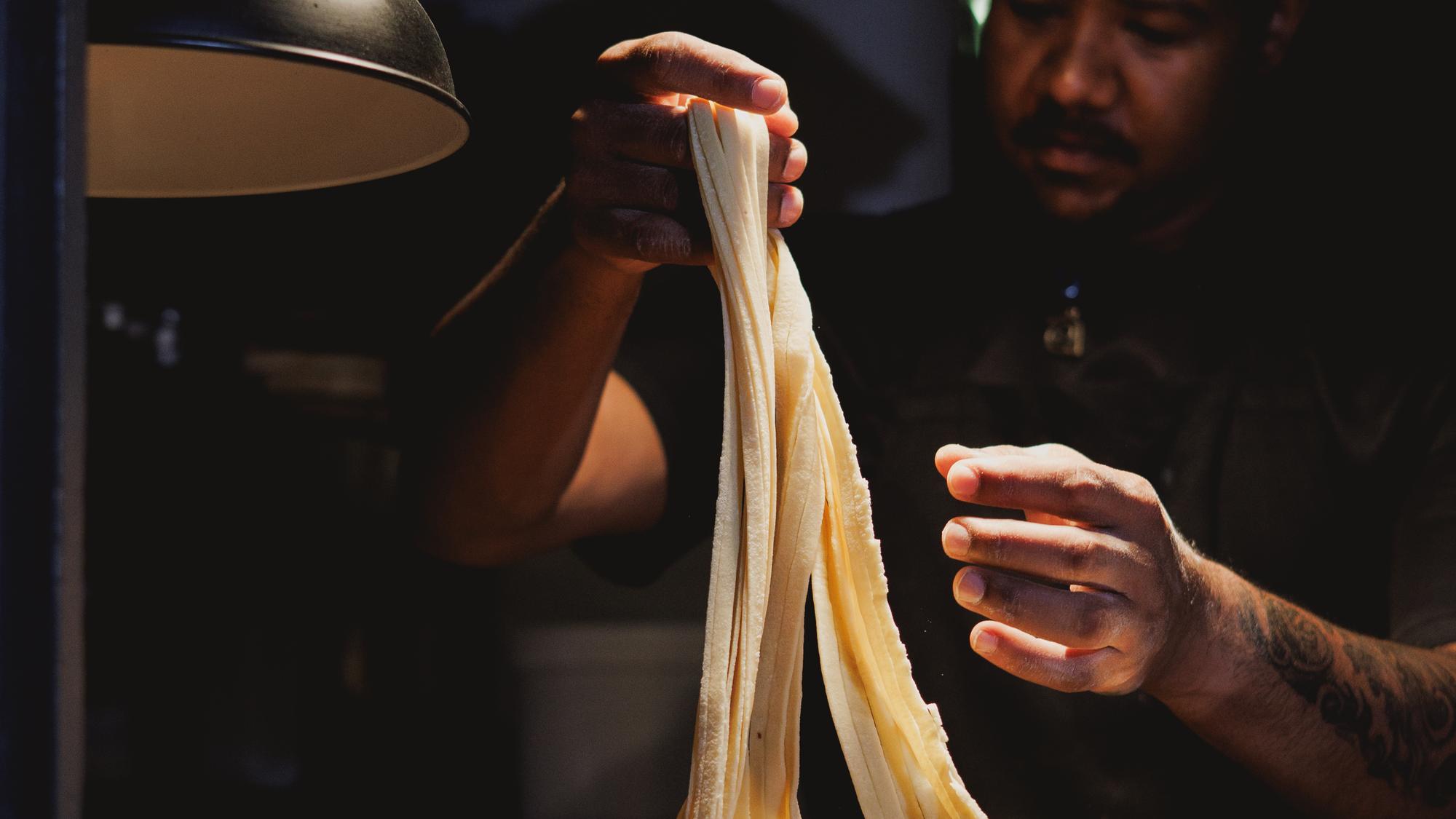 Sheets of fresh pasta being pulled by hand under the kitchen lamps